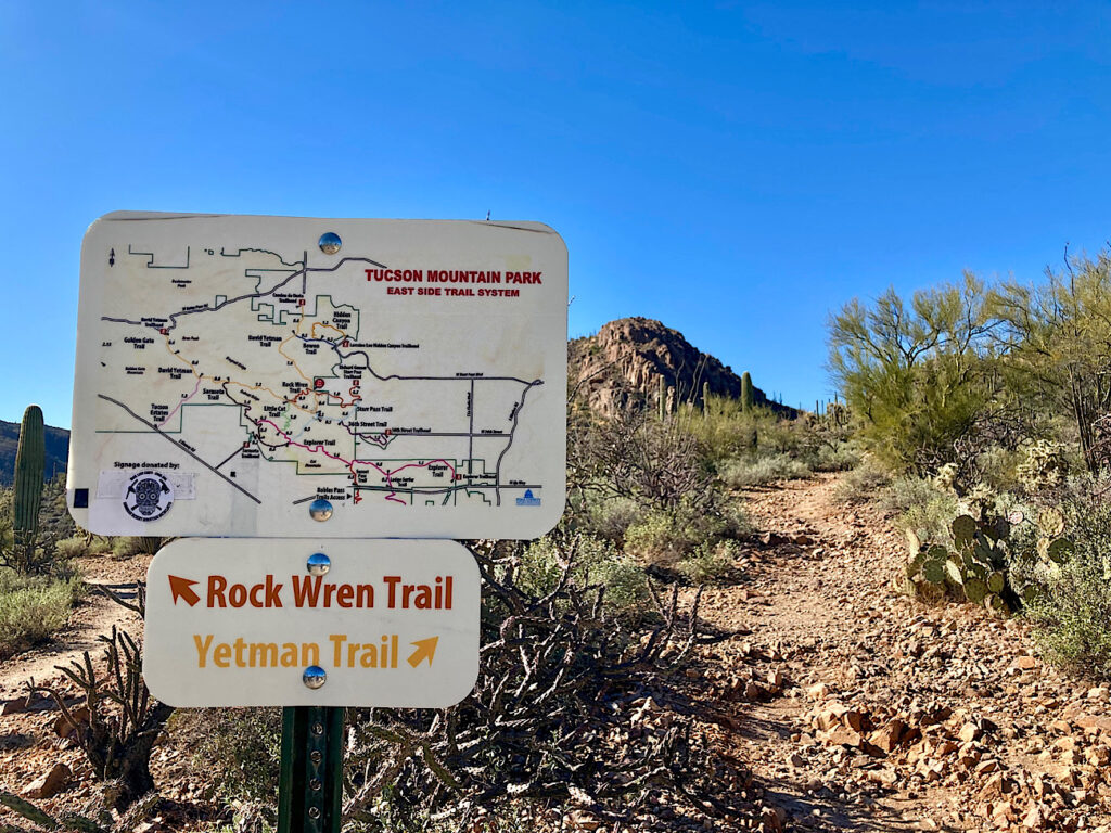 Trail sign in desert pointing left to Rock Wren trail and right to Yetman trail.