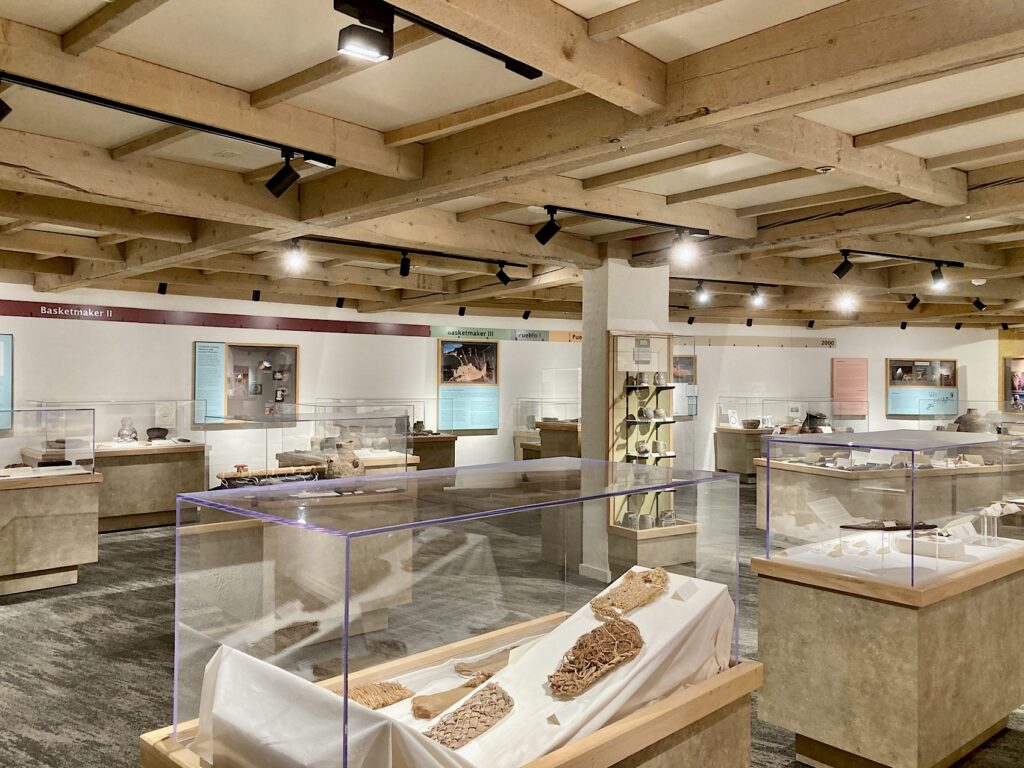 Museum displays in glass cases under exposed wood beam ceiling.