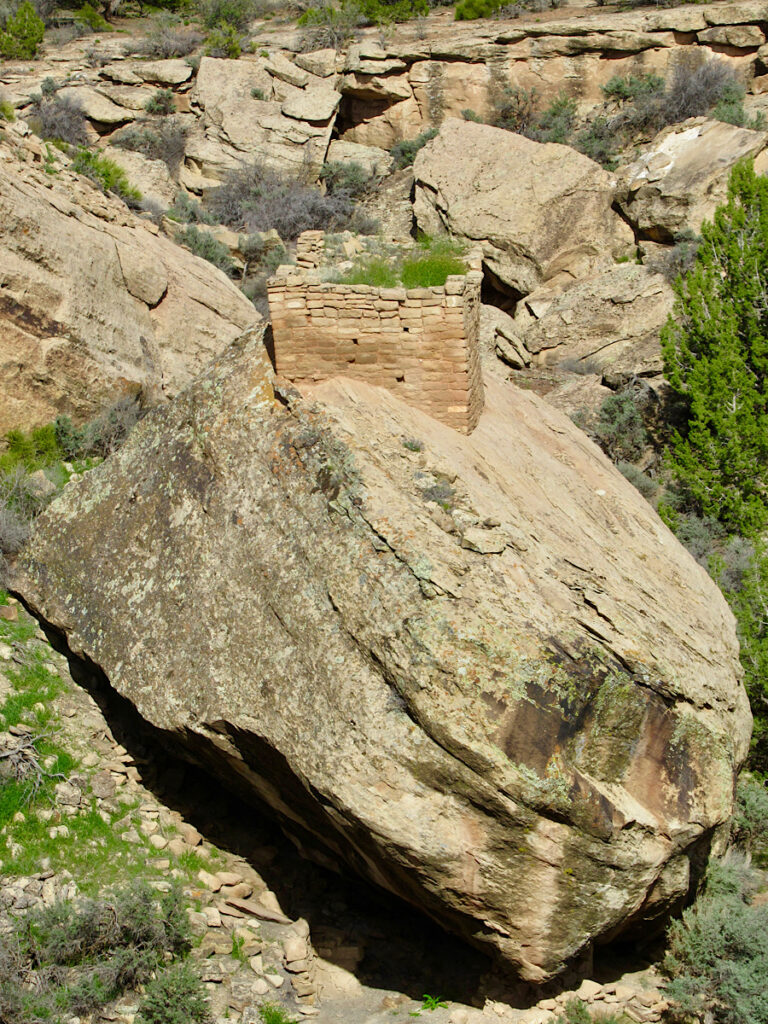 Square stone building flowing across the top of a massive, uneven boulder in the valley bottom.