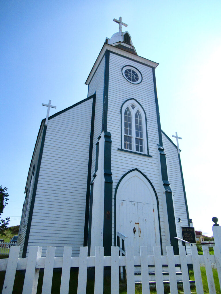 Vertical image of white wooden church with blue accent trim and white picket fence in front.