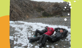 "There's no such thing as bad weather just bad clothes" text on lime green and light orange background with central photo of three people in rain gear lying on a pebble beach with chunks of ice.