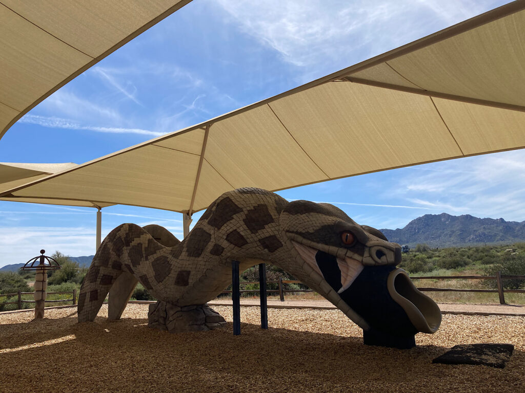 Play structure shaped like a rattlesnake under white canvas tarps in campground.
