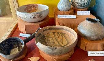Six pieces of pottery, some black on white, some red on white and one black on orange in display case.