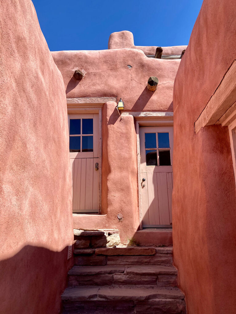 Narrow staircase between two pink adobe walls leading up to a set of white-painted wood doors.