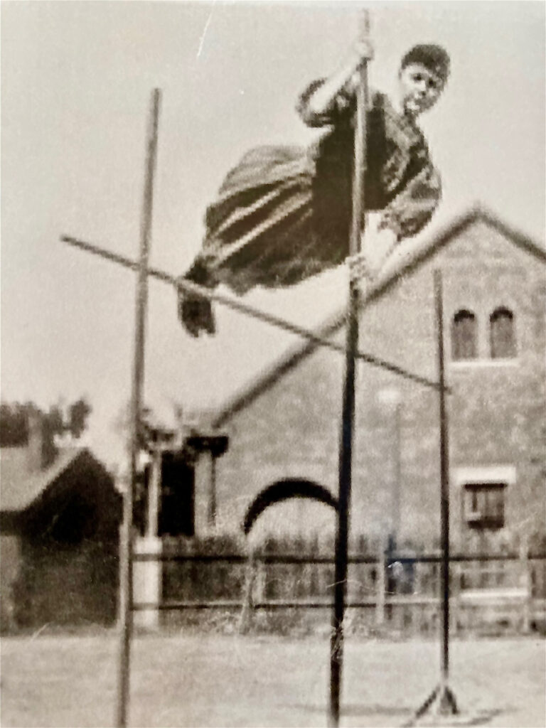 Historic black and white photograph of a woman pole vaulting.