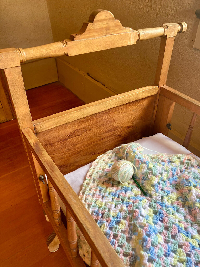 Old-fashioned wooden cradle with knitted multi-coloured, pastel blanket inside.
