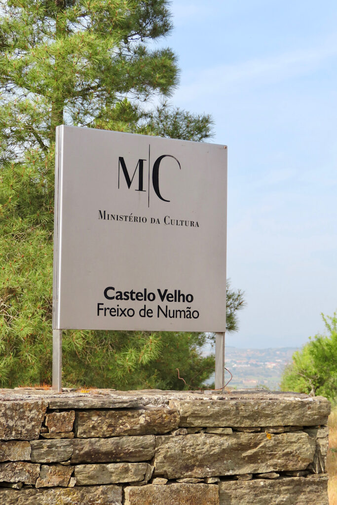 White entrance sign with black lettering reading: "Minister da Cultura. Castelo Velho. Freixo de Numáo."