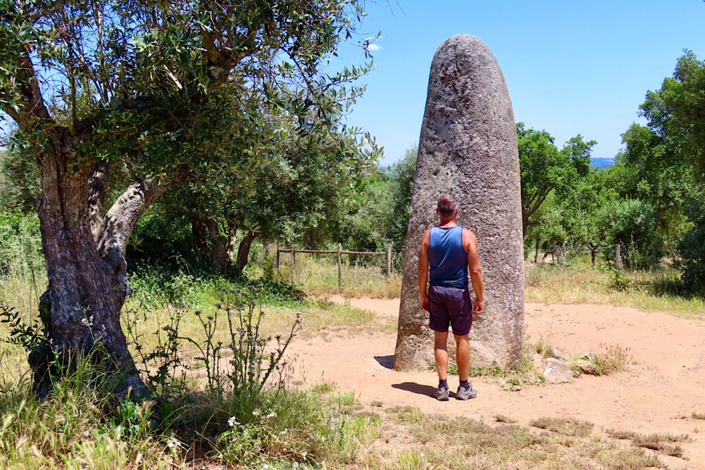 Man facing large standing stone that towers above his height. 