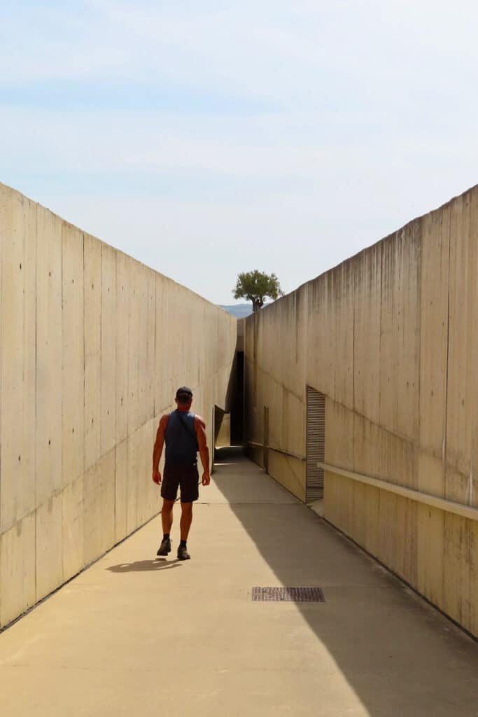 Man in dark shorts and short-sleeved shirt walking down a concrete path way between concrete walls.