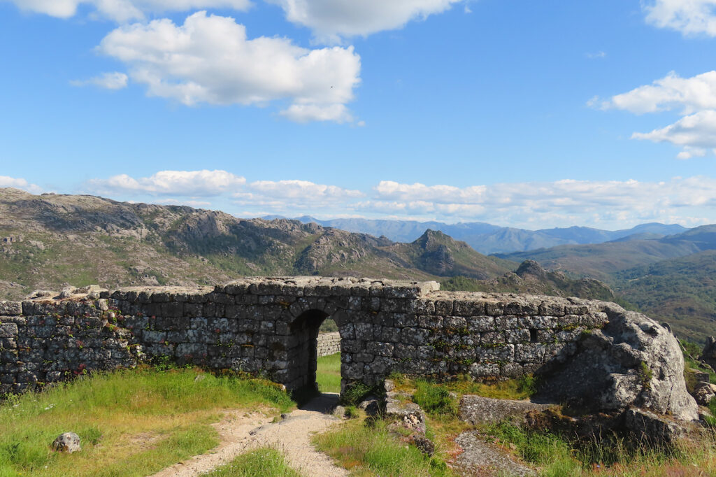 Stone wall with doorway in centre on ridge overlooking mountain valleys.all under blue sky with a few white clouds.