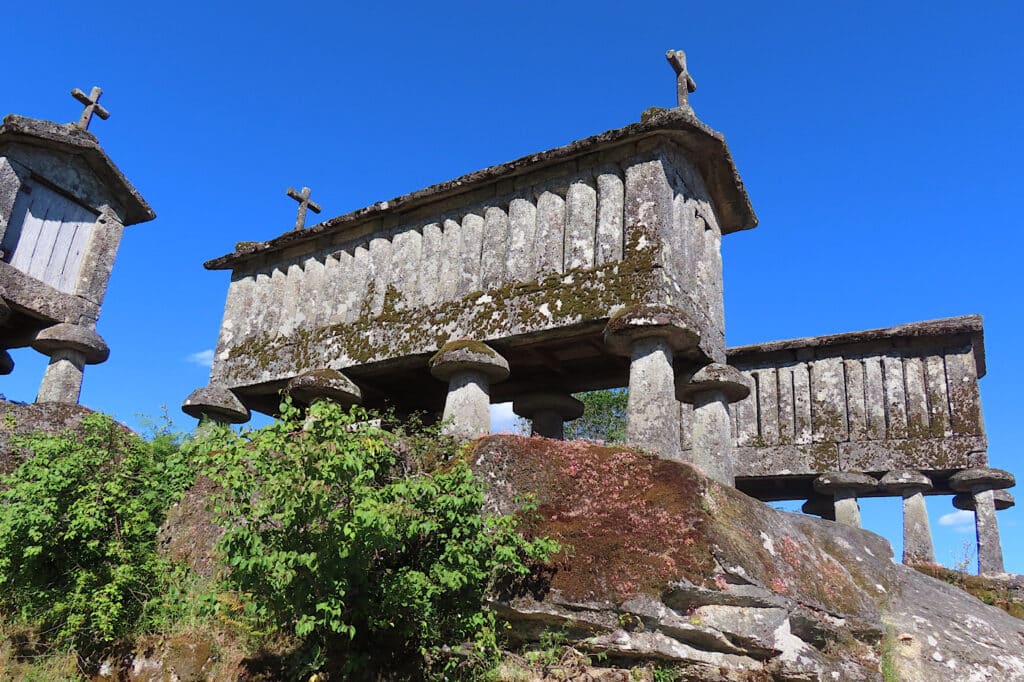 Three rectangular stone buildings on stilts high on cliff under blue sky.