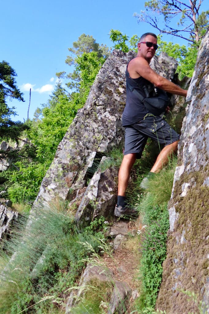 Man in short-sleeved shirt and shorts climb up rocky trail.