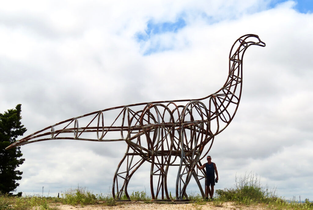 Metal sculpture of a dinosaur towering above a man. 