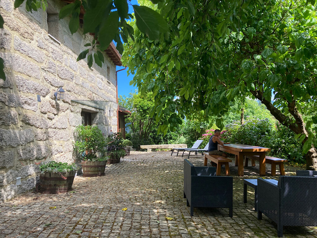 Stone house in background with large patio and man sitting at wooden table.