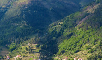 Lush green rolling mountains above red-roofed and whitewashed building in valley bottom.