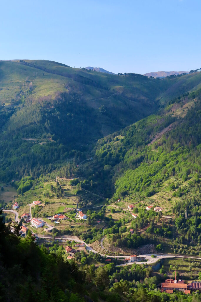 Lush green rolling mountains above red-roofed and whitewashed building in valley bottom.