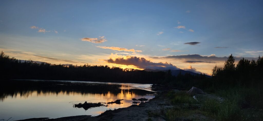 Sun setting with silhouette of trees alongside a river.