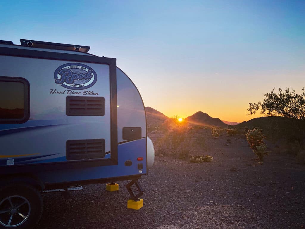 Blue and white trailer in foreground with reddish orange glow of sunset behind.