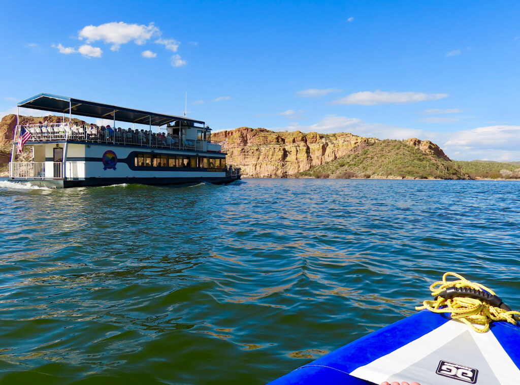 Large cruise boat on lake with front end of blue and white inflatable boat in bottom corner of photo.