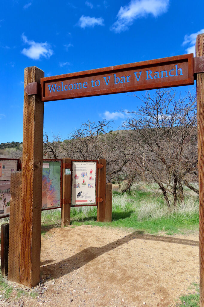 Metal sign raised on tall poles under blue sky. Sign reads: Welcome to V Bar V Ranch.