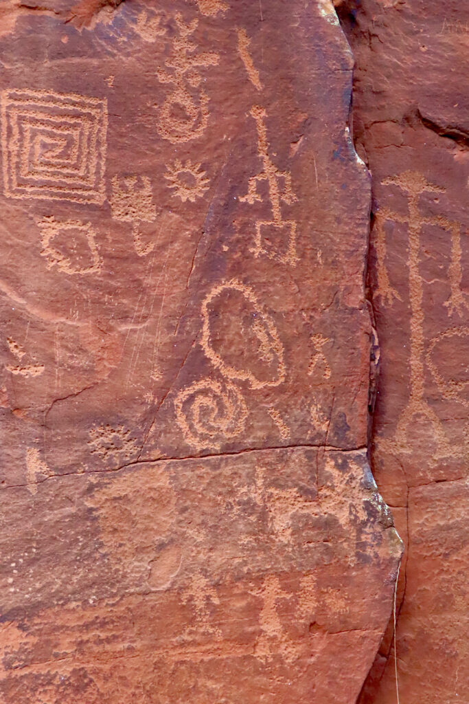 Rock art etched into reddish rock with images of animals, spirals and human-type figures.