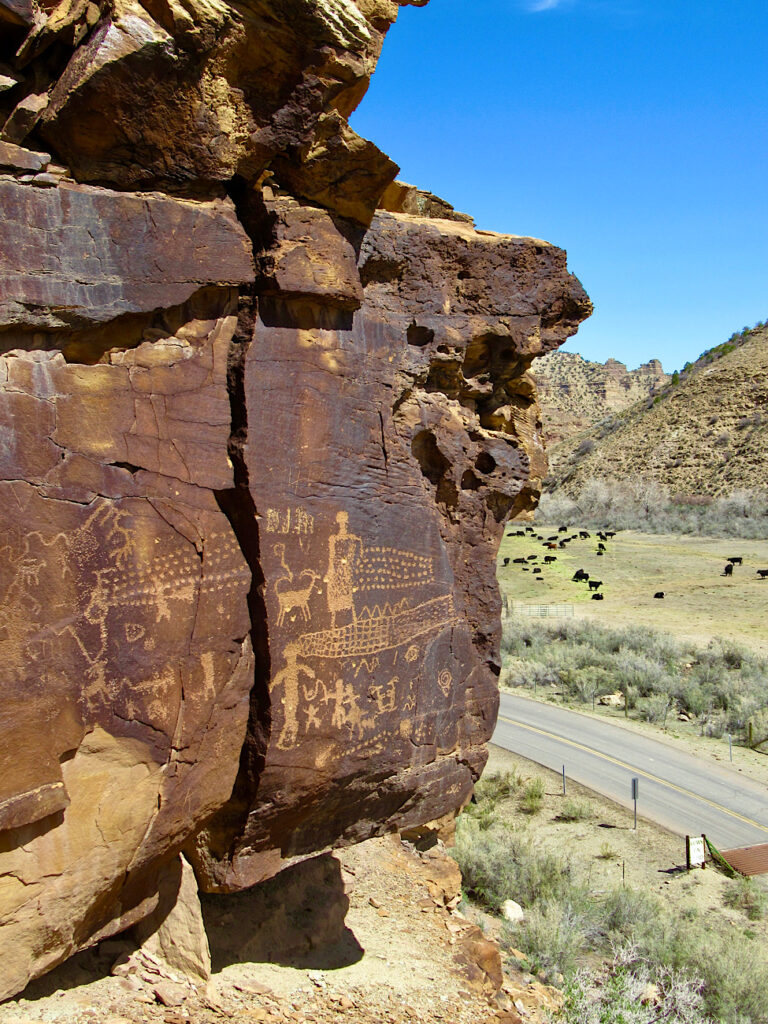 Image of rock art on red sandstone cliff high above a green field in a valley.