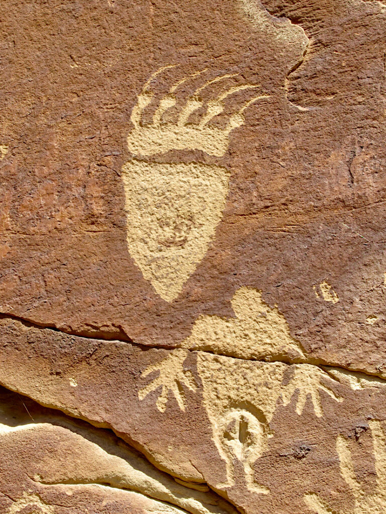 Images of a bear track and an anthropomorphic figure carved into red sandstone rock.