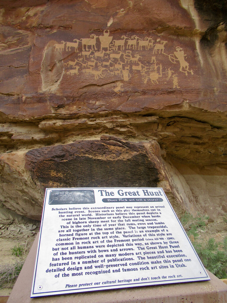 Rock art panel on red  sandstone wall with white interpretive sign below describing the images.