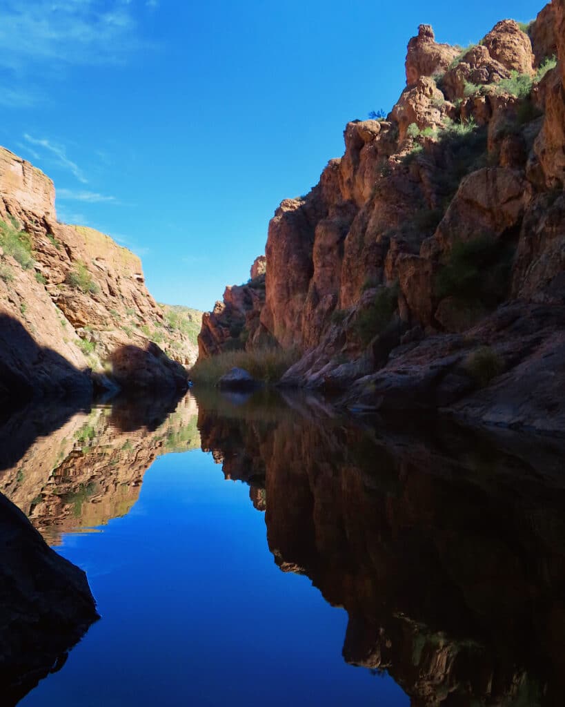 Red rock canyon reflecting on still water under blue sky.