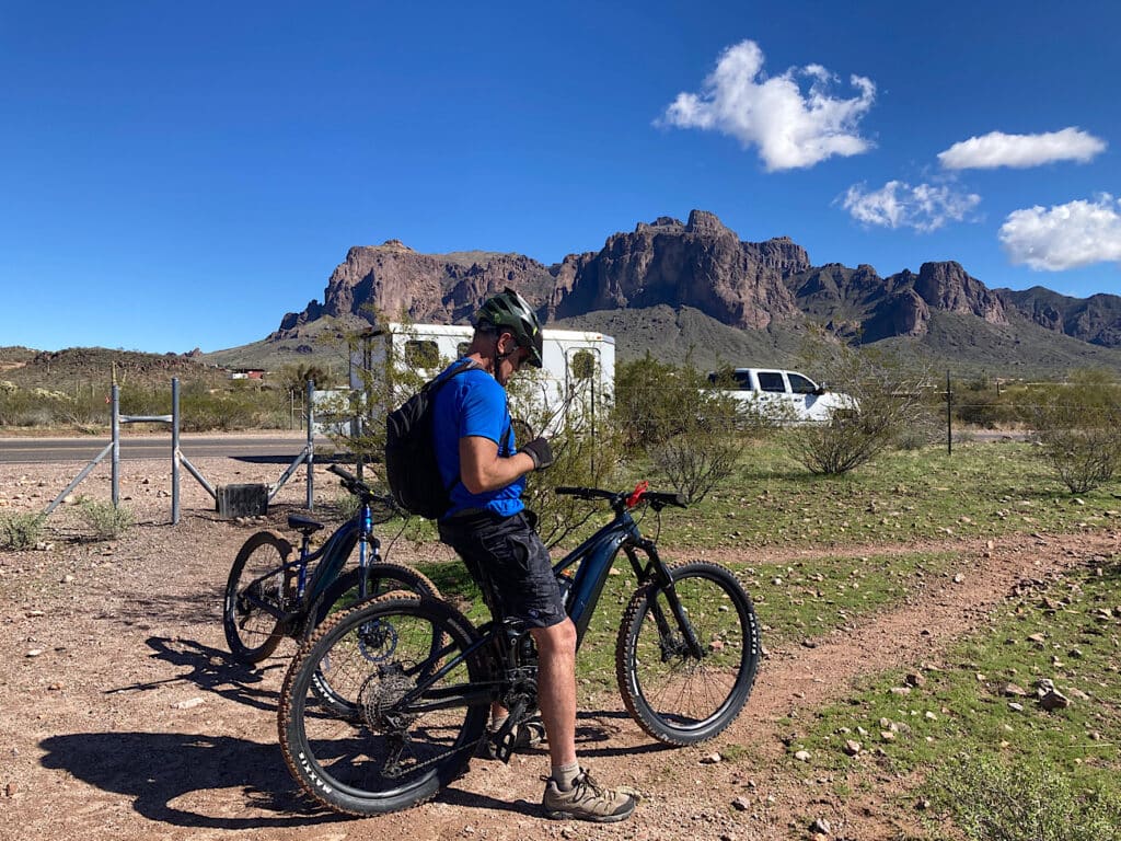 Man in black shorts, bicycle helmet and blue shirt sitting astride mountain bike on a trail.