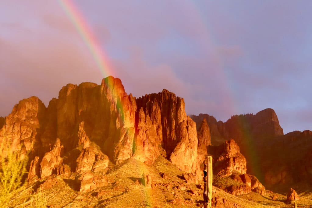 Rainbow in mist with orange glowing light on rugged mountain.