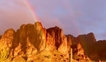 Rainbow in mist with orange glowing light on rugged mountain.