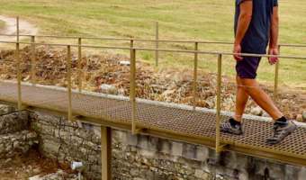 Pin image for TimeTravelTrek.com post of man walking on raised walking above ruins. Text reads: Travel Adventures Exploring Roman Ruins in Conimbriga Portugal.