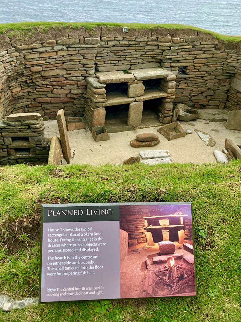 Interpretive sign at Skara Brae above a subterranean room describing "planned living."