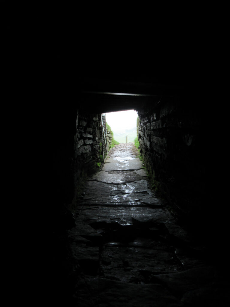 Dark, rock-lined passage with white light at entrance.