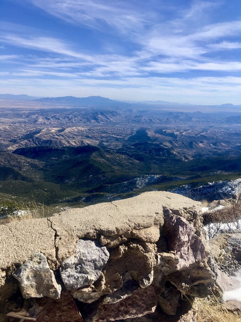 View of old cement and rock wall above rugged landscape below.