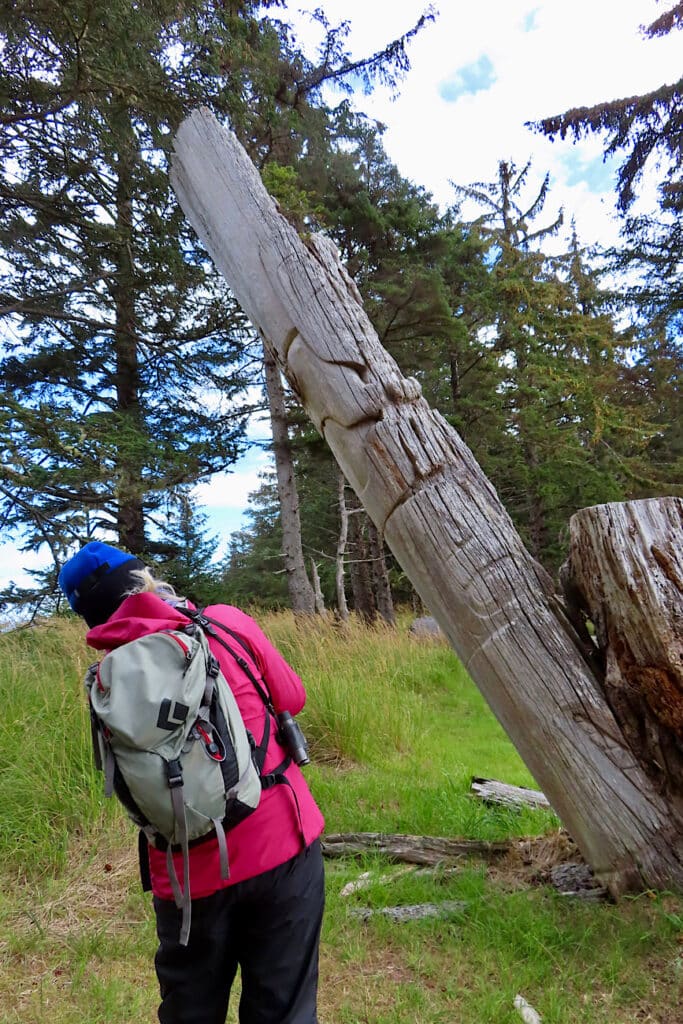 Woman in pink jacket and dark pants leaning over to check out leaning totem pole.