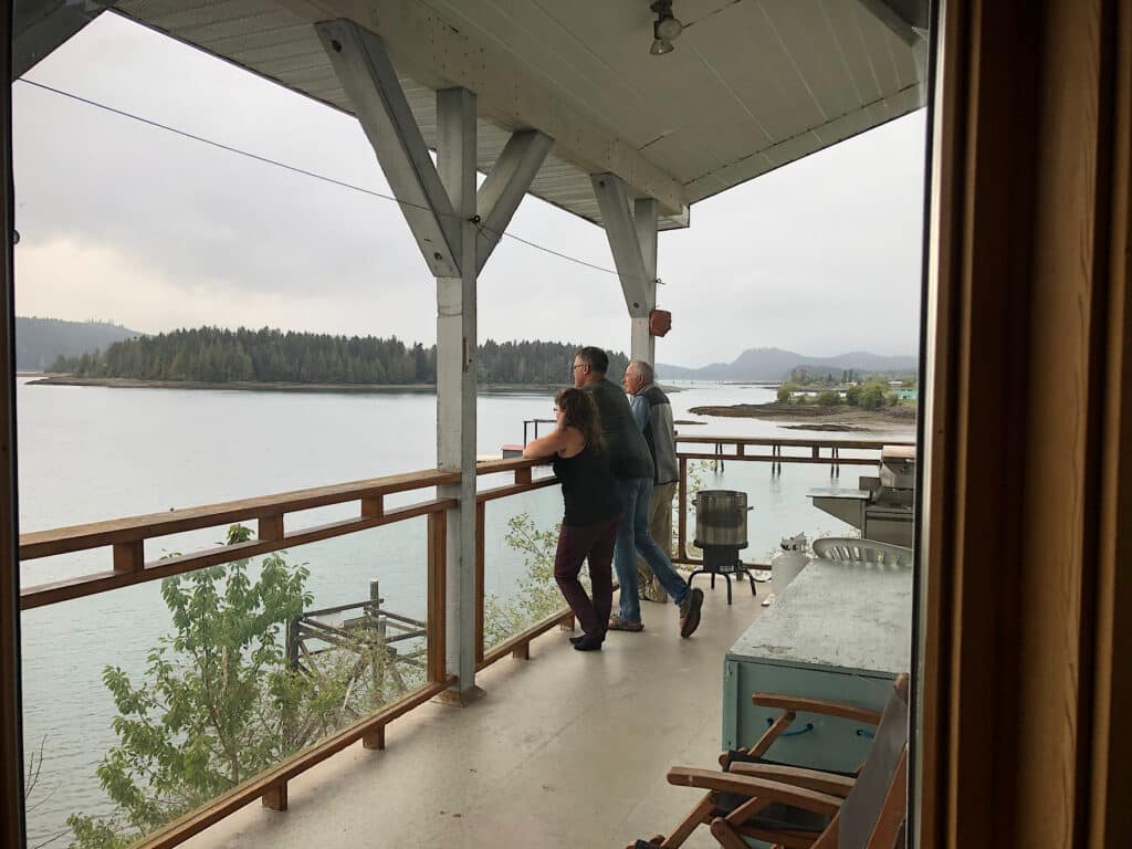 Two men and a woman standing on a covered balcony overlooking water.