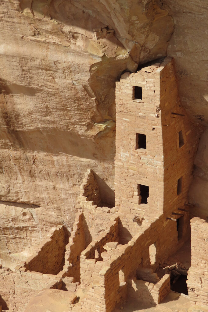 Multi-storey high square stone building with 3 windows on front built against high sandstone cliff face.