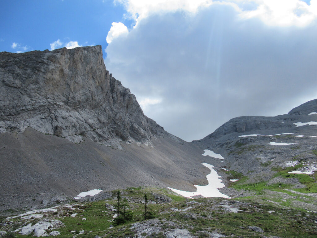 Rugged grey peaks rising above green alpine meadows with patches of snow.