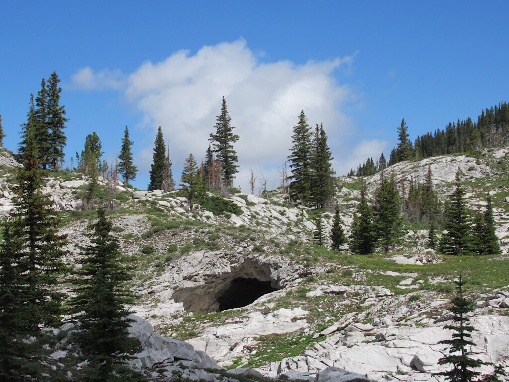 Rugged, rocky terrain with small dark cave entrance visible.