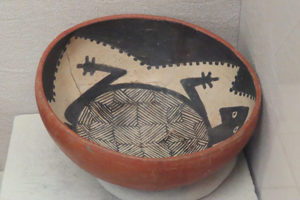 Red bowl set in display case painted with black-and-white image of a patterned turtle inside.