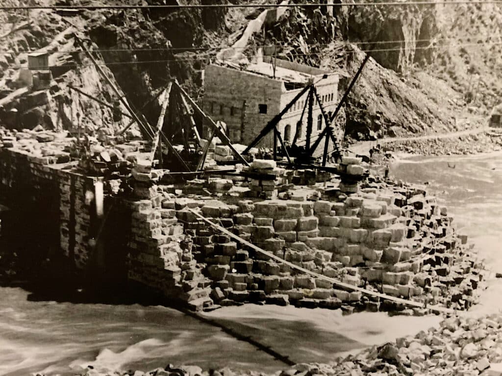 Black and white image of large stone blocks being placed to form a large rock dam.