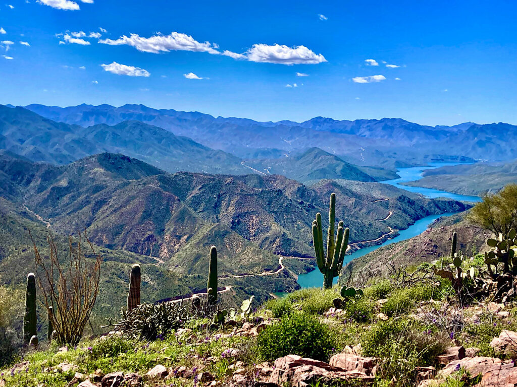 View from high ridge overlooking narrow, turquoise lake and surrounding hills.