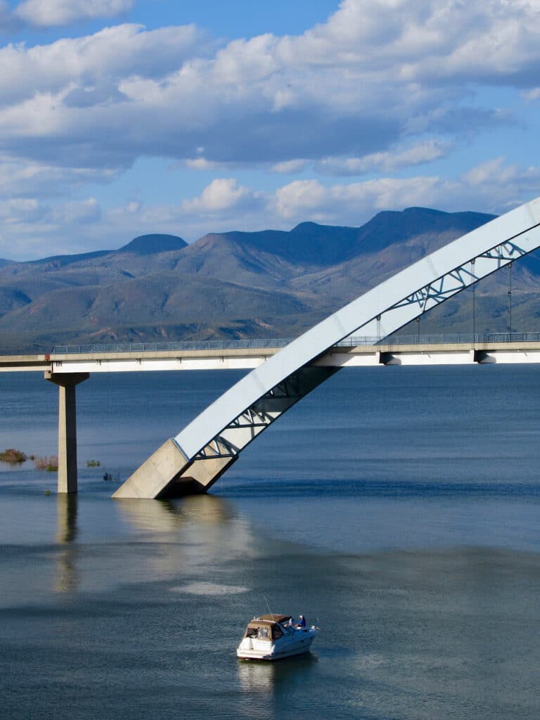 Large curved metal bridge over water with boat in foreground.