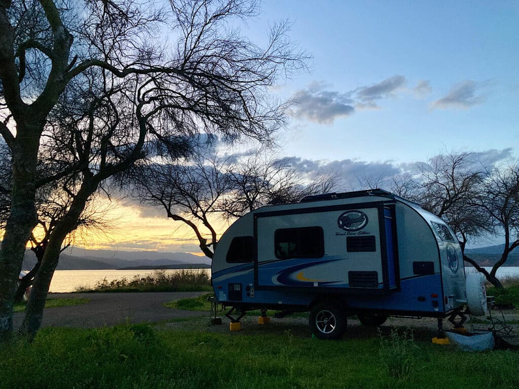 Blue and white trailer parking in a campsite overlooking a lake at twilight.