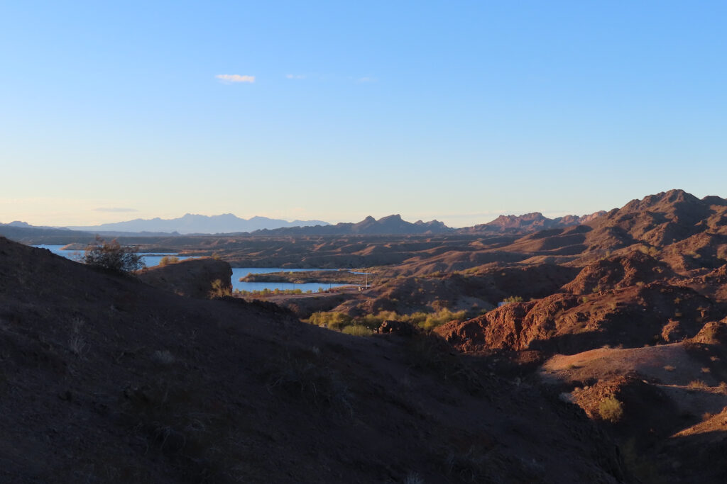 Evening light on brown hills above a distant lake.