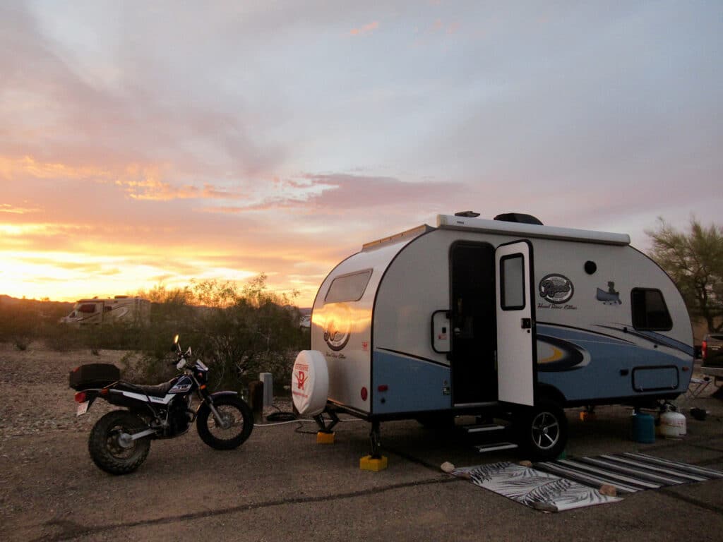 Blue and white trailer and motorcycle in sunset light.