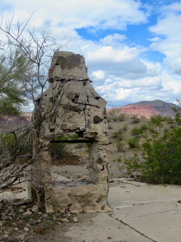 Stone chimney and cement slabs in front of distant mountain under partially cloudy sky.