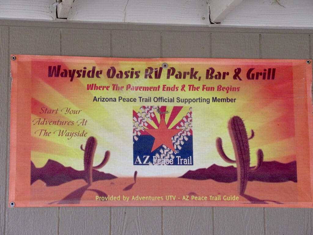 Banner for Wayside Oasis RV Park, Bar, & Grill with glowing sunset and cactus image.